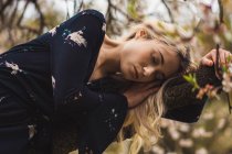 Junge blonde Frau lehnt sich an blühenden Baum und entspannt sich mit geschlossenen Augen in der Natur — Stockfoto