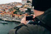 Turista masculino tomando fotos de la ciudad vieja con teléfono inteligente, Oporto, Portugal - foto de stock