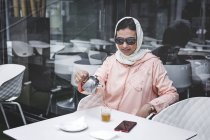 Марокканка с хиджабом и типичным арабским платьем, наливающим чай в кафе — стоковое фото