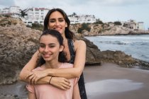 Жінка обіймає усміхнену дочку на морському фоні влітку — стокове фото