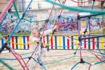 Fröhliches kleines Mädchen klettert auf Spielplatz an Seilen hoch — Stockfoto
