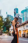 Mujer asiática en ropa elegante caminando por la calle iluminada al atardecer - foto de stock