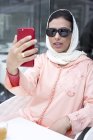 Elegante mujer marroquí con hijab y vestido árabe típico tomando selfie en la cafetería - foto de stock