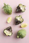 Fresh halved artichokes and pieces of lemon on pink background — Stock Photo