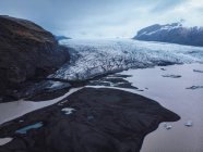 Verschneites Tal mit Fluss und Bergen unter wolkenverhangenem Himmel, Island — Stockfoto