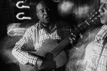 Músico tocando la guitarra y cantando en el club nocturno, tiro en blanco y negro con larga exposición - foto de stock