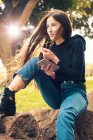 Young woman sitting on rock and holding smartphone in park — Stock Photo
