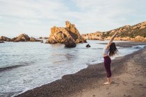 Fitte Frau dehnt sich am felsigen Strand — Stockfoto