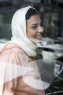 Smiling Moroccan woman with hijab sitting behind window pane — Stock Photo