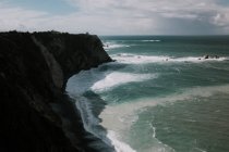 Vista a la roca costera y el océano azul ondulado en día nublado. - foto de stock