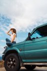 Woman sitting on car trunk and looking away at seaside — Stock Photo