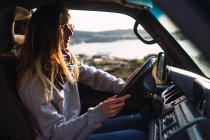 Молода жінка в сонцезахисних окулярах за кермом автомобіля в природі — стокове фото