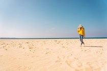 Femme en pull jaune vif debout sur la plage de sable — Photo de stock