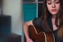 Jeune femme jouant de la guitare à la maison — Photo de stock