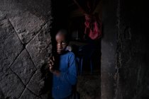 ANGOLA - ÁFRICA - 5 de abril de 2018 - Menino africano de pé à entrada da casa grunhida e olhando para a câmera — Fotografia de Stock