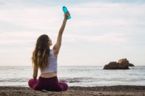 Сидя на пляже, женщина держит бутылку в руках — стоковое фото