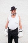 Homem adulto em chapéu e luvas de boxe branco na parede áspera. — Fotografia de Stock