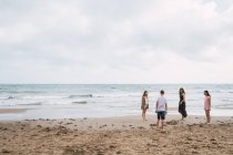 Mujer y adolescentes caminando en la playa de arena - foto de stock