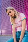 Блондинка позує сидячи на різнокольоровій стіні і дивлячись на камеру — стокове фото