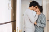 Young couple in pajamas standing and kissing in doorway at home — Stock Photo
