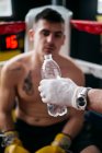 Crop hand giving bottle of water to boxer sitting in ring. — Stock Photo