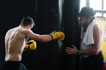 Erwachsenentrainer steht und hält Boxsack für Sportler im Fitnessstudio. — Stockfoto