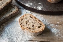 Tranche de pain frais appétissant dans la farine sur une table en bois rugueux — Photo de stock