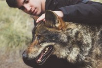Junger Mann streichelt Wolf im Zoo — Stockfoto