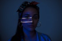 Jolie femme debout dans une pièce sombre avec deux petites lignes lumineuses sur le visage — Photo de stock