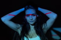 Молода приваблива жінка з червоною лінією на обличчі та тілі дивиться на камеру на темному фоні — стокове фото
