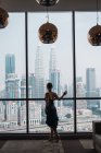 Woman standing at window in apartment and looking at skyscrapers — Stock Photo