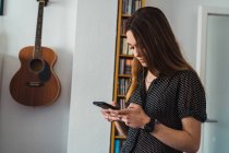 Молода жінка стоїть вдома і переглядає смартфон — стокове фото