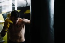 Боксер без рубашки в перчатках стоит и бьет грушу во время тренировки. — стоковое фото