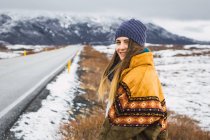 Mulher em roupas quentes em pé na natureza fria na beira da estrada — Fotografia de Stock