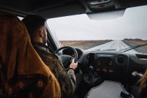 Vista posteriore dell'uomo che guida l'auto lungo la strada remota nelle pianure dell'Islanda in una giornata piovosa e cupa. — Foto stock