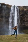 Glückliches Mädchen springt auf Schanze gegen Wasserfall, Island — Stockfoto