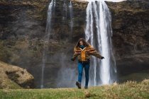 Жінка ходить перед водоспадом з витягнутими руками — стокове фото
