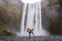 Donna in piedi in asana su ghiaia con cascata sullo sfondo, Islanda — Foto stock