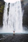 Excited man with arms up standing in front of waterfall — Stock Photo
