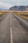 Strada asfaltata in pianura con alte montagne sullo sfondo, Islanda — Foto stock