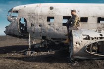 Вид сбоку на молодого мужчину, сидящего на старом разбитом самолете на открытом воздухе и смотрящего в сторону — стоковое фото