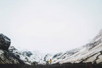 Frau in gelber Jacke steht in der Nähe verschneiter Berge — Stockfoto