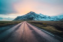 Straße im Grünen und verschneite Berge bei Sonnenaufgang — Stockfoto