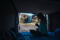 Mulher sentada no acolhedor caminhão de acampamento segurando copo na cachoeira da frente — Fotografia de Stock