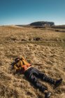 Homem barbudo em roupas quentes deitado na grama seca no campo — Fotografia de Stock