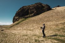 Homem com capuz casaco com câmera em pé no vale em tempo ensolarado, Islândia — Fotografia de Stock