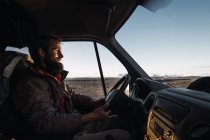 Улыбающийся бородатый мужчина за рулем автомобиля на природе — стоковое фото