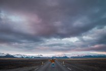 Mulher de pé na estrada no campo com montanhas no fundo — Fotografia de Stock