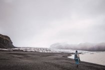 Donna che cammina sulla costa con montagne innevate sullo sfondo — Foto stock