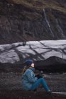 Mulher sentada na costa fria com areia preta — Fotografia de Stock
